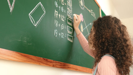 Back view of african student answer question while writing at board. Teacher looking at elementary student doing math quiz in front of classroom while smart children attend in math lesson. Pedagogy.の写真素材