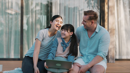 Father, mother and daughter focus laptop at terrace with garden view outside house. Parent use outdoor activity to communicate young generation about environment care cross generation gap. Divergence.の写真素材