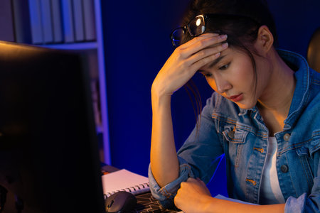 Stressful young beautiful asian creative looking on pc to search project creator social media online with planning channel strategy reach of more viewer home at neon modern office at night. Stratagem.の写真素材