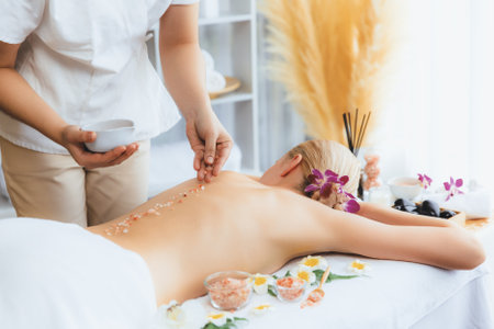 Woman customer having exfoliation treatment in luxury spa salon with warmth candle light ambient. Salt scrub beauty treatment in health spa body scrub. Quiescentの写真素材