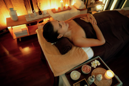 Caucasian woman customer enjoying relaxing anti-stress spa massage and pampering with beauty skin recreation leisure in warm candle lighting ambient salon spa at luxury resort or hotel. Quiescentの写真素材