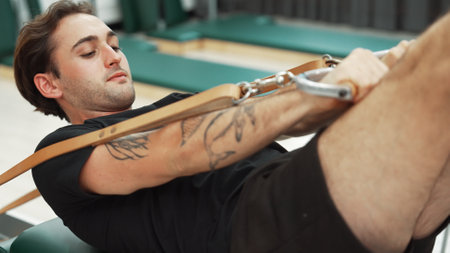 Man performing core strengthening exercise using pilates reformer. Close up of happy trainer workout pilates while posing on reformer with hundred pose for strengthening arm and shoulder. Habituate.の写真素材