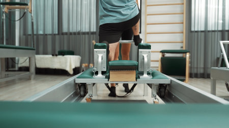 Man practicing kneeling stretch on pilates reformer with assistance to improve flexibility and strength. Trainer assist student doing lunge stretch on the reformer for enhancing balance. Habituate.の写真素材