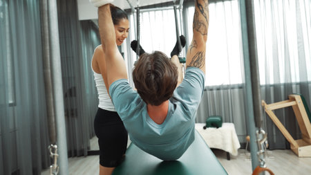 Healthy client practicing inverted leg raise on Pilates Cadillac under instructor guidance. Man hanging back stretch on the cadillac for improving core strength, and upper body stability. Habituate.の写真素材