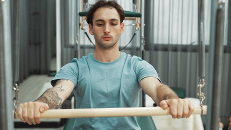 Man performing seated core exercise on pilates trapeze holding bar to strengthen arms and core muscles at gym. Trainer doing chest press on the cadillac for strengthening chest, shoulder. Habituate.の写真素材