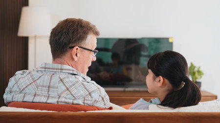 Grandfather and granddaughter together watch interesting entertainment media on TV. Old senior use technology communicate with young generation cross generation gap strengthen family bond. Divergence.の写真素材
