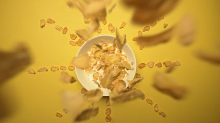 Top view of dropping cereal in bowl of milk with yellow background. Slow motion of cornflakes breakfast cereal putting in white bowl. Healthy food. Aerial view. Morning energy, concept. Comestible.の写真素材