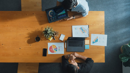 Top view of project manager working on laptop while colleague show report or financial graph from...