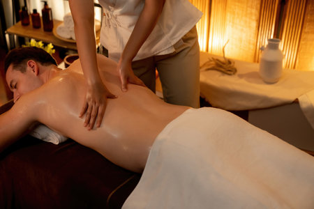 Caucasian man customer enjoying relaxing anti-stress spa massage and pampering with beauty skin recreation leisure in warm candle lighting ambient salon spa at luxury resort or hotel. Quiescentの写真素材