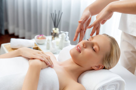 Caucasian woman enjoying relaxing anti-stress head massage and pampering facial beauty skin recreation leisure in dayspa modern light ambient at luxury resort or hotel spa salon. Quiescentの写真素材