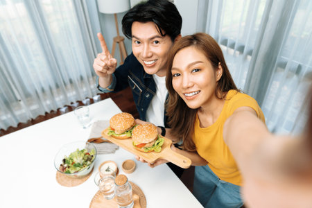 Top view of smiling host chef influencers taking photo with smartphone by selfie holding double hamburger on cooking show special easy with salad side dish homemade on social media channel. Infobahn.の写真素材