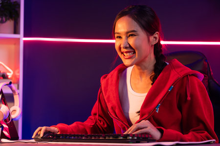 Host channel of gaming beautiful Asian girl streamer with smiling face playing online game media on pc, looking on social online gamer. Esport skilled team players in neon blue modern room. Stratagem.の写真素材