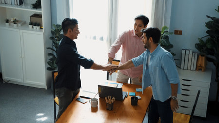Top view of creative marketing team with casual cloth looking at laptop while shaking hands together for greeting or making contract or agreement at business meeting with sticky notes. Convocation.の写真素材