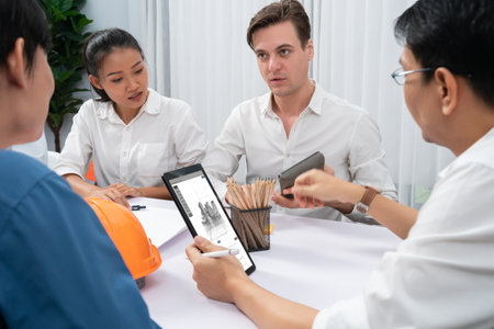 Diverse group of civil engineer and client working together on architectural project, reviewing construction plan and building blueprint using tablet at meeting table. Prudentの写真素材