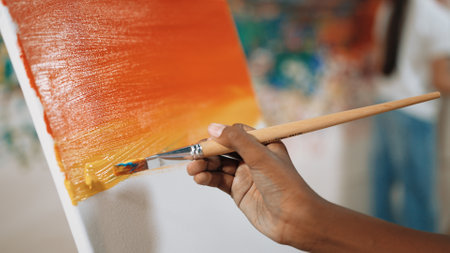 Closeup of african boy hand paint canvas with warm tone color while caucasian girl in casual outfit drawing cool tone colors behind at colorful stained wall. Creative activity concept. Edification.の写真素材