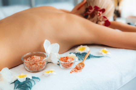 Woman customer having exfoliation treatment in luxury spa salon with warmth candle light ambient. Salt scrub beauty treatment in health spa body scrub. Quiescentの写真素材