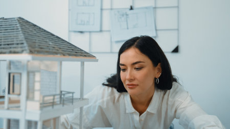 Young beautiful caucasian architect engineer turns house model around to inspect house construction and check mistake point to solve the problem on meeting table at modern office. Closeup. Immaculate.の写真素材