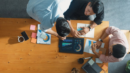 Executive manager explain financial graph to colleague at meeting room. Top aerial view of diverse marketing team sharing idea and planning strategy while sitting at table with tablet. Convocation.の写真素材