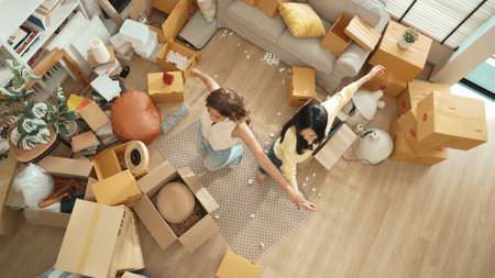 Happy lesbian lover dancing together at living room in moving day. Couple of friend moving to music and perform freestyle dancing at living room with cardboard box scattering. Relocation. Myrmidon.の写真素材