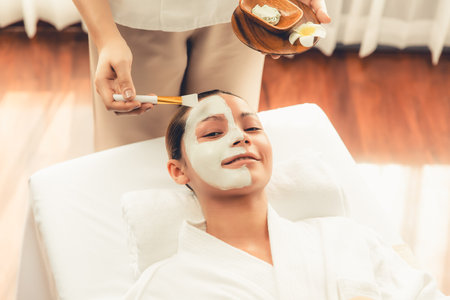 Serene ambiance of spa salon, woman customer indulges in rejuvenating with luxurious face cream massage with modern daylight. Facial skin treatment and beauty care concept. Quiescentの写真素材
