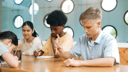 Smart boy listening teacher explain while lecturing and think about idea. Diverse student study or learning together in classroom while writing idea or taking a note. Creative education. Edification.の写真素材