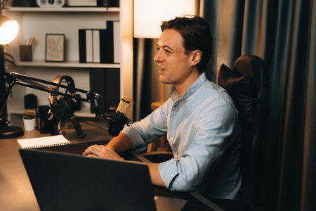 Host channel smart broadcaster talking on live social media application searching on laptop, broadcasting streamer wearing headphone using mic at modern home office studio in warm lighting. Pecuniary.の写真素材