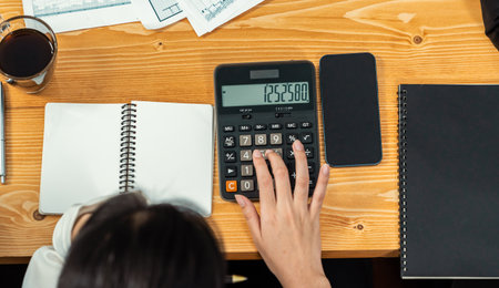 Businesswoman working on wooden office workspace desk, calculating financial report. Business accountant manage corporate budget, tracking income and expense accounting using calculator. Meticulousの写真素材