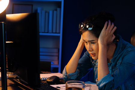 Stressful young beautiful asian creative looking on pc to search project creator social media online with planning channel strategy reach of more viewer home at neon modern office at night. Stratagem.の写真素材