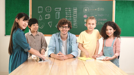 Professional caucasian teacher and diverse student looking at camera while happy school boy smiling. Group of multicultural children smiling while standing in front of classroom. Education. Pedagogy.の写真素材