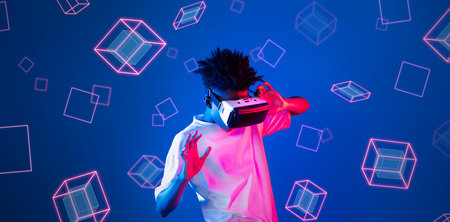 Smart boy standing at blue background while floating geometric shape. African man playing game and...