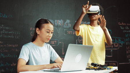 African boy wear headset to enter in metaverse while young beautiful academic student writing, coding, programing system on table with laptop or device placed. innovative education. Edification.の写真素材
