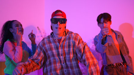 Hispanic hipster wear colorful cloth and waving to freestyle music. Professional break dancer moving to lively beat with neon light and led light with modern studio surrounded by friend. Regalement.の写真素材