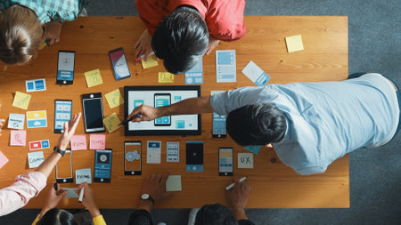 Top view of software developer team looking Ux Ui design for mobile phone interface from tablet while comparing and planning wireframe prototype designing together at creative workplace. Convocation.の写真素材