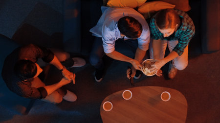 Top aerial view of caucasian father and mother watching movie while eating snack with friend. Happy family with colleague looking at television while dad hold snack bowl at living room. Convocation.の写真素材