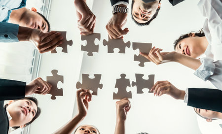 Multiethnic business people holding jigsaw pieces and merge them together as effective solution solving teamwork, shared vision and common goal combining diverse talent. Below view. Habilimentの写真素材