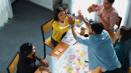 Top view of creative start up team giving high five to encourage their teamwork or successful project while making scrum task board for managing workflow by using marker and sticky notes. Convocation.の写真素材