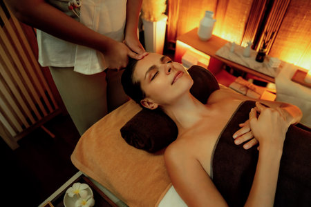 Caucasian woman enjoying relaxing anti-stress head massage and pampering facial beauty skin recreation leisure in warm candle lighting ambient salon spa in luxury resort or hotel. Quiescentの写真素材