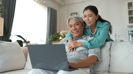 Senior businessman working at laptop while grandmother supporting him. Stressed elder man looking at financial chart or deceasing sales report from computer while elder woman hugging him. Myrmidon.の写真素材