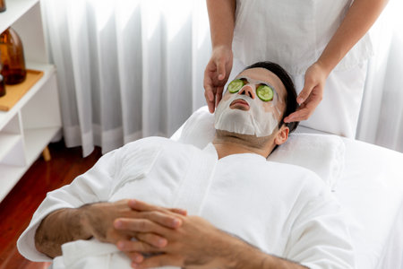 Serene daylight ambiance of spa salon, man customer indulges in rejuvenating with luxurious cucumber facial mask. Facial skincare treatment and beauty care concept. Quiescentの写真素材