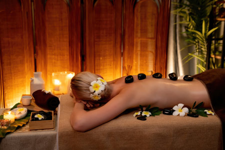 Hot stone massage at spa salon in luxury resort with warm candle light, blissful woman customer enjoying spa basalt stone massage glide over body with soothing warmth. Quiescentの写真素材