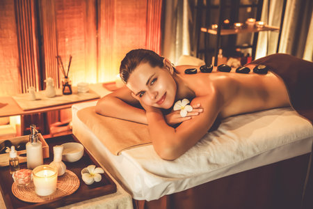 Hot stone massage at spa salon in luxury resort with warm candle light, blissful woman customer enjoying spa basalt stone massage glide over body with soothing warmth. Quiescentの写真素材