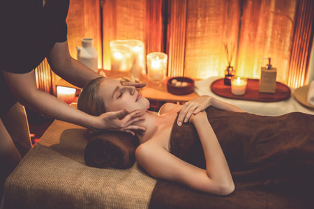 Caucasian woman enjoying relaxing anti-stress head massage and pampering facial beauty skin recreation leisure in warm candle lighting ambient salon spa in luxury resort or hotel. Quiescentの写真素材