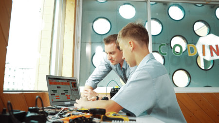 Smart student present coding program and car model to skilled teacher. Teenager using computer to programing system for robotic machines at table with electronic equipment scatter around. Edification.の写真素材