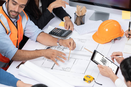 Diverse group of civil engineer and client working together on architectural project, reviewing construction plan and building blueprint at meeting table. Prudentの写真素材