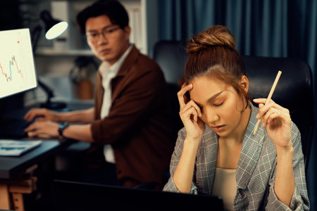Serious face of thinking businesswoman focusing computer to report data analysis social media online project job with coworker working at back side at over late night time at modern office. Infobahn.の写真素材