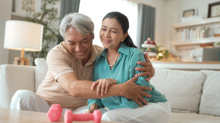 Grandmother holding dumbbell while encouraging and hugging her wife. Happy elder couple doing dumbbell exercise for enhancing flexibility or improving cardiovascular. Preventive healthcare. Myrmidon.の写真素材