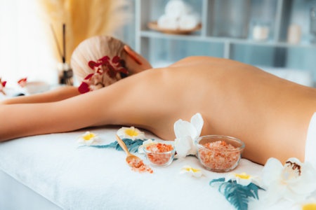 Woman customer having exfoliation treatment in luxury spa salon with warmth candle light ambient. Salt scrub beauty treatment in health spa body scrub. Quiescentの写真素材