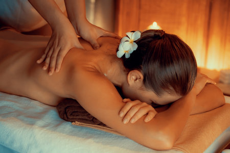 A person receiving a relaxing anti-stress spa massage and pampering with beauty skin recreation leisure in warm candle lighting ambient salon spa at luxury resort or hotel.の写真素材