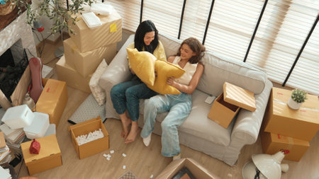 Top view of friends playing pillow fight while sitting at sofa in living room on moving day....