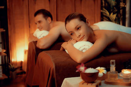 Caucasian couple customer enjoying relaxing anti-stress spa massage and pampering with beauty skin recreation leisure in warm candle lighting ambient salon spa at luxury resort or hotel. Quiescentの写真素材